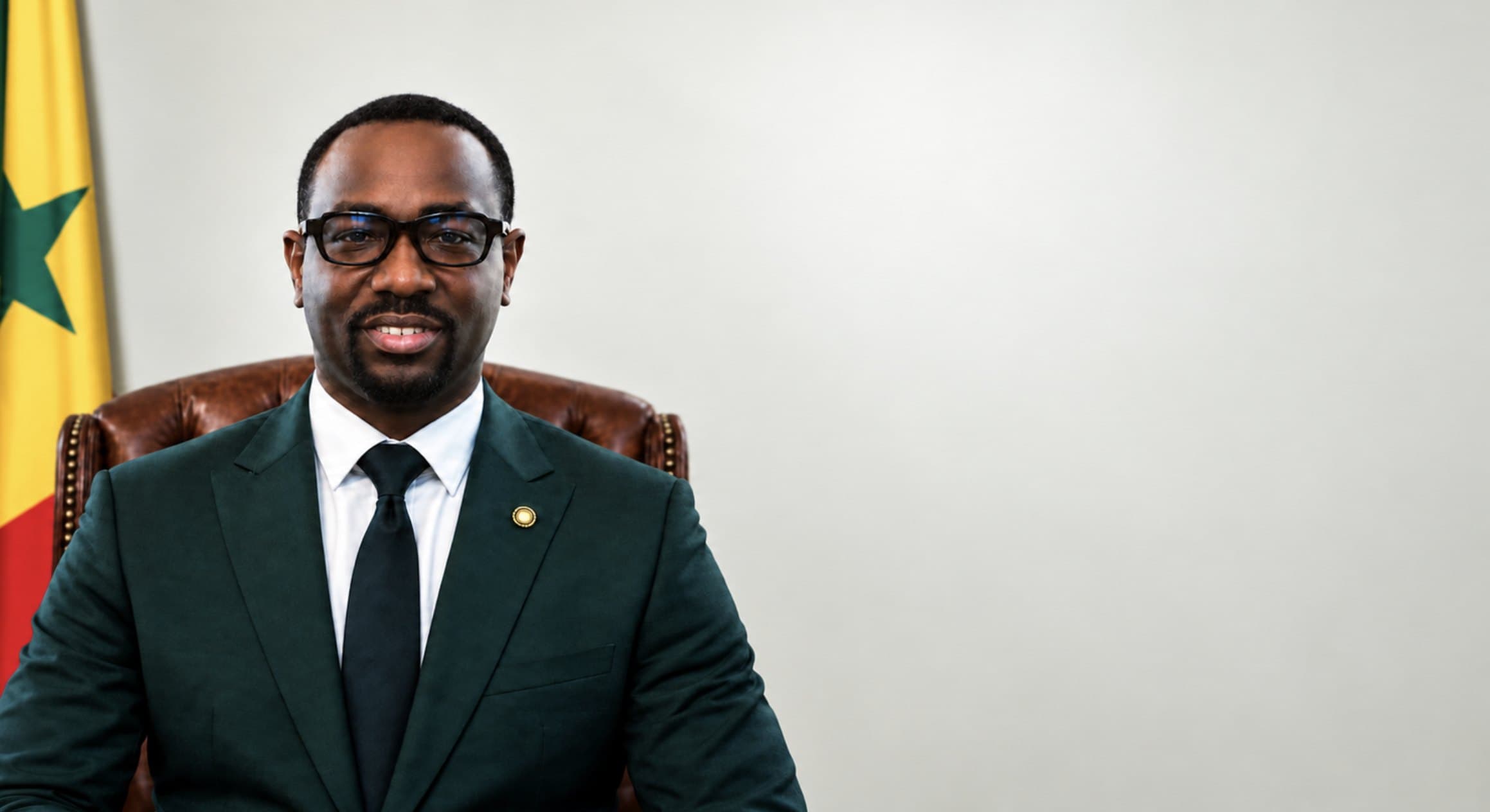 Matar Diène, en costume vert, assis dans son bureau devant le drapeau sénégalais